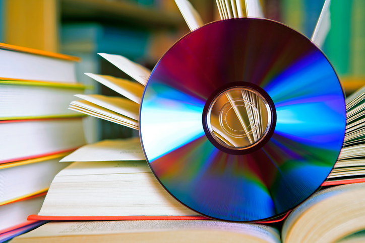 A DSLR photo of an open book with a CD in front of it. Some other books are visible at the background. Shallow depth of field. Can illustrate the concept of digital audio books instead of standard paper books. book to film adaptations