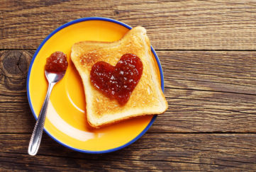 Toast bread with jam in shape of hearts on vintage wooden table. Top view. Happiness is like a jam sandwhich