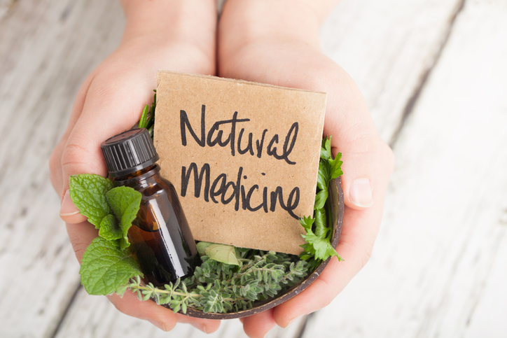 home remedies Bowl of herbs and essential oil and card saying Natural Medicine on light floor boards