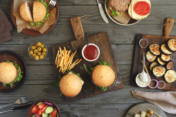 Different food on a wooden table, burgers, fries, grilled eggplant, salad, different sauces and olives, top view. Outdoors food Concept. lovely leaving lunch