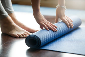 Close-up of attractive young woman folding blue yoga or fitness mat after working out at home in living room. Healthy life, keep fit concepts. Horizontal shot. Go