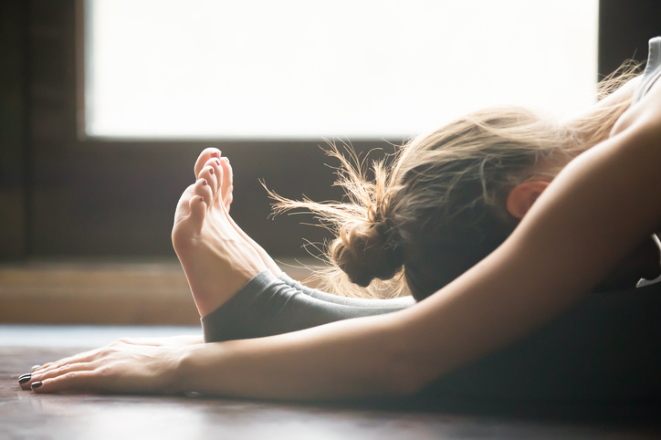 Young woman practicing yoga, sitting in Seated forward bend exercise, paschimottanasana pose, working out, wearing sportswear, grey pants, bra, indoor, home interior background, close up. stretch