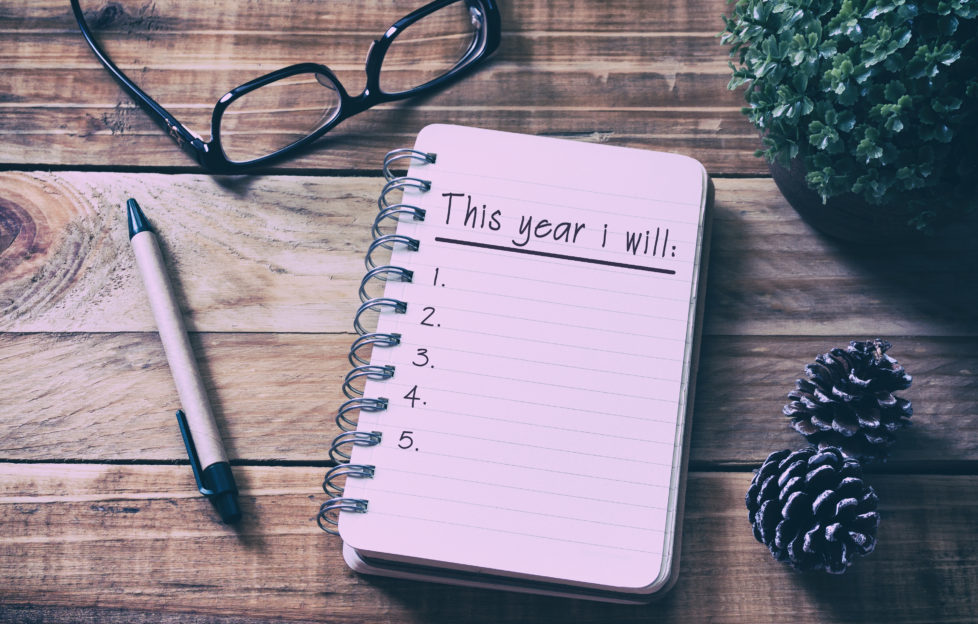 A notepad on the table with 'This year I will' written on top of a numbered list, next to a pair of glasses and pen