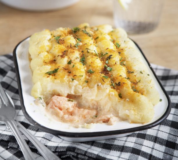 Fish pie in blue and white dish on a checked cloth with cutlery beside it.