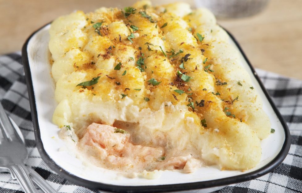 Fish pie in blue and white dish on a checked cloth with cutlery beside it.