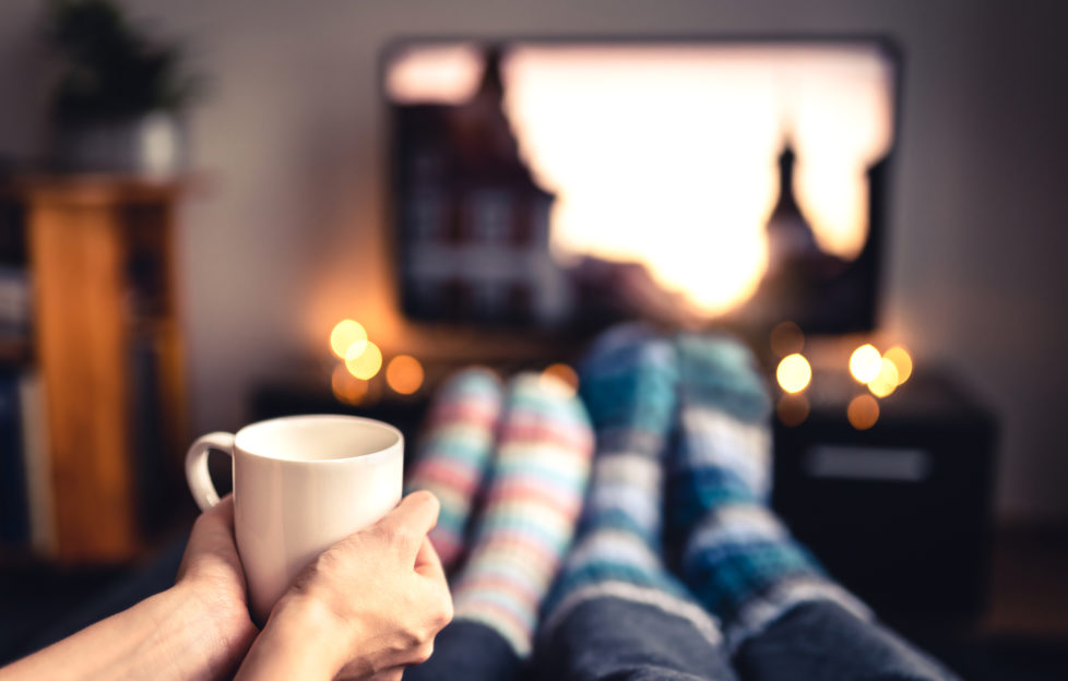 Couple drinking tea, hot chocolate, eggnog or mulled wine and watching tv in warm cozy woolen socks in winter. Woman holding cup of morning coffee in home living room. Sick people with flu.