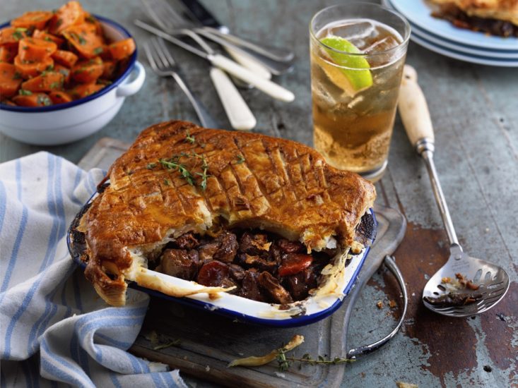 Crabbie's Ginger Beer steak pie in a blue and white dish with a glass of ginger beer, ice and lime on the side.