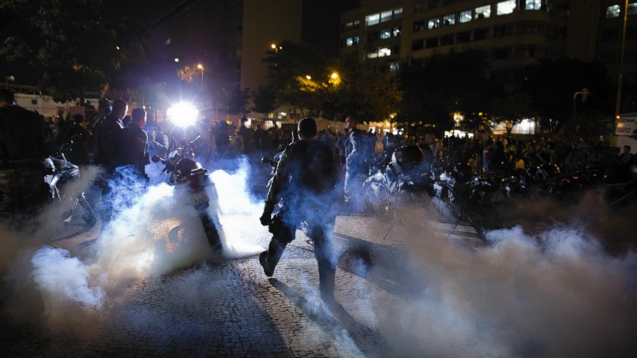 Police officers walk through a cloud of tear gas during a protest against the money spent on the World Cup preparations, in Rio de Janeiro, Brazil,