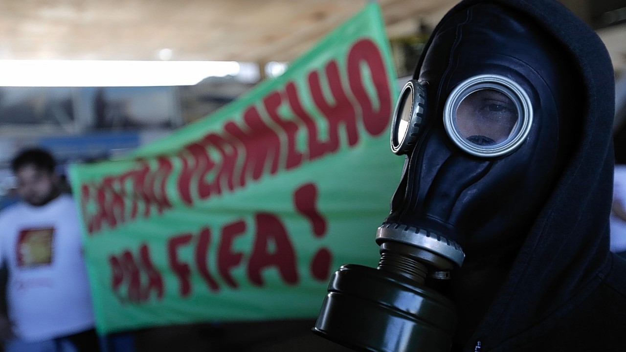 A man with a gas mask stands next to a banner that reads in Portuguese, "Red Card for FIFA",  during a protest against the money spent on the World Cup, in Brasilia, Brazil,