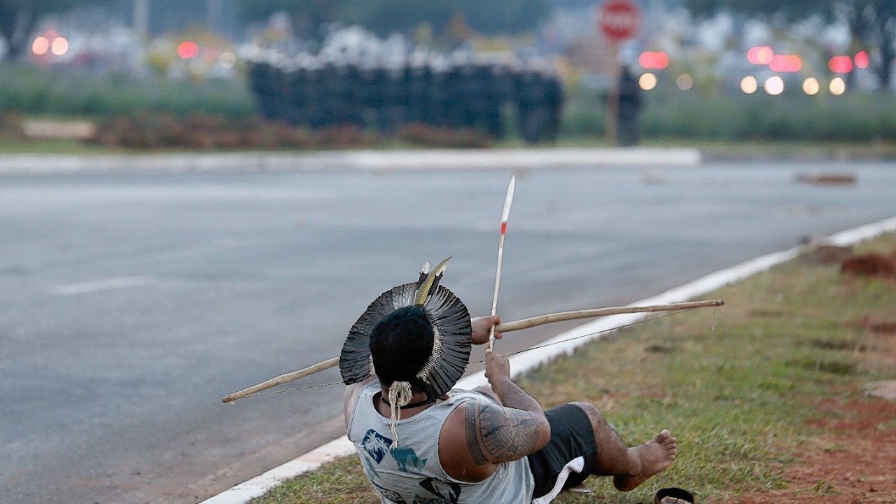 An Indigenous protester in traditional headdress gets ready to fire an arrow against the military police during a protest against the FIFA World Cup outside the National Stadium in Brasilia, Brazil