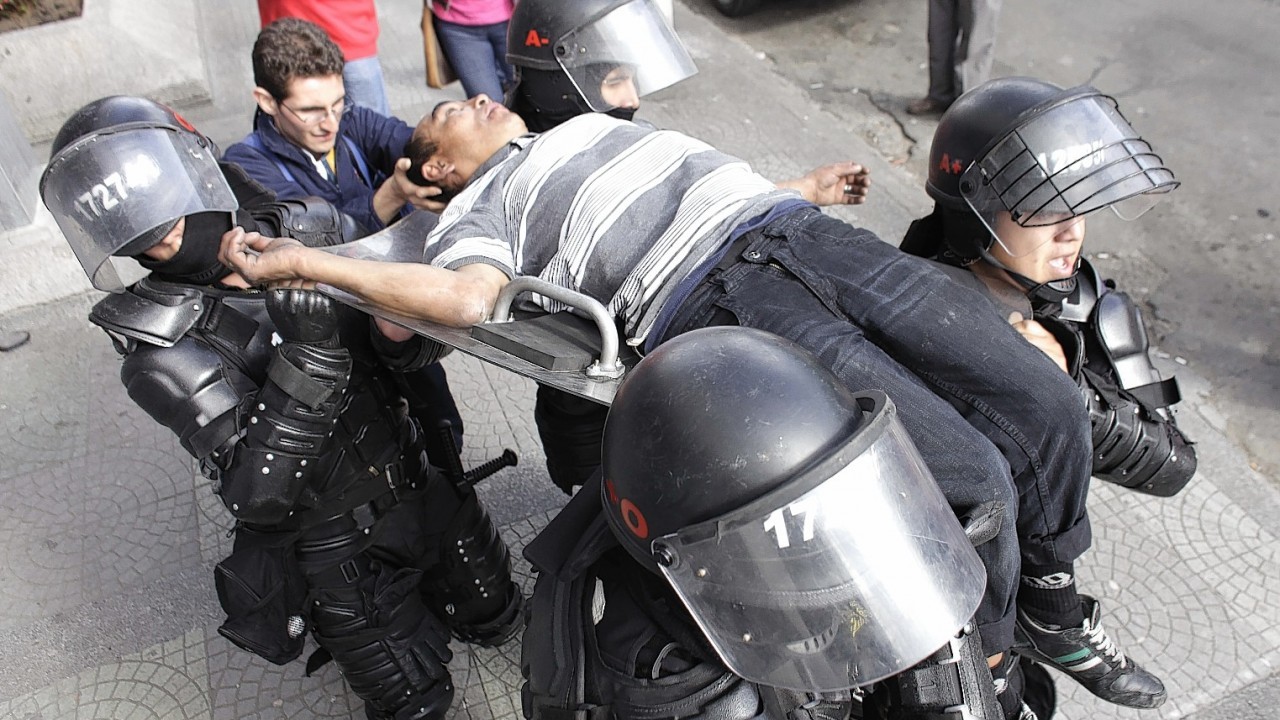 Riot police carry a passerby who fainted due to the tear gas thrown by the police as they dispersed a group of hooded students who blocked the avenue in front of the National University in Bogota