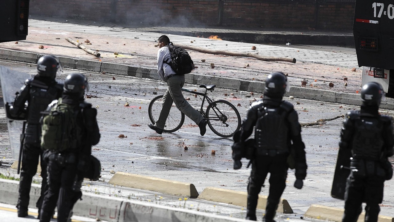 A cycler runs by with his bike, past a group  police as they dispersed a group of hooded students who blocked the avenue in front of the National University in Bogota, Colombia,