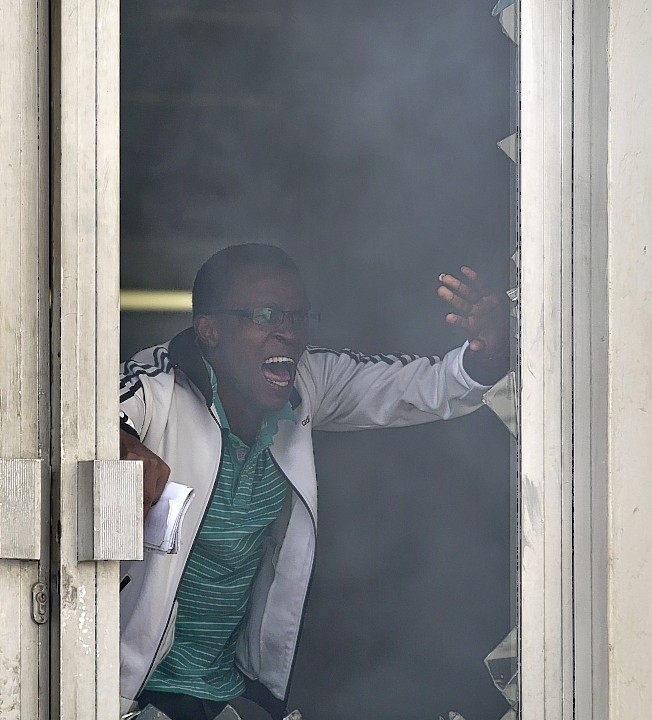 A student or member of university staff tries to escape from a tear-gas-filled building, before being chased back inside by riot police, inside Nairobi University's main campus in downtown Nairobi,