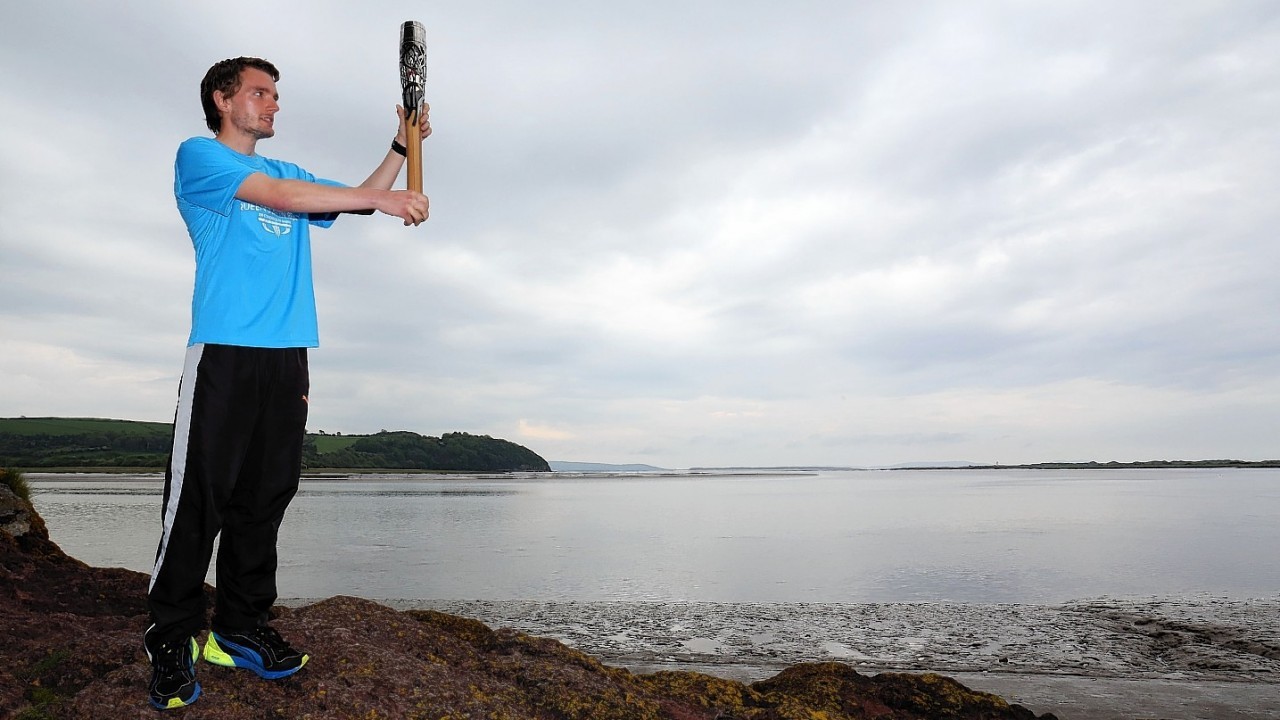 Queen's Baton relay of Baton Bearer Dewi Griffiths holding the Queen's Baton looking out across the Taf Estuary near the Dylan Thomas writing shed at Laugharne in Wales