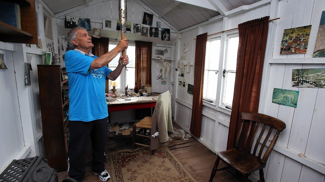 Baton Bearer John Phillips holding the Queen's Baton inside the Dylan Thomas writing shed at Laugharne in Wales. Wales is nation 68 of 70 nations and territories the Queen's Baton will visit