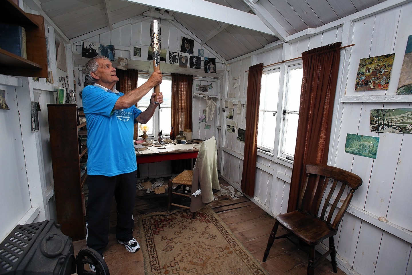 Baton Bearer John Phillips holding the Queen's Baton inside the Dylan Thomas writing shed at Laugharne in Wales. Wales is nation 68 of 70 nations and territories the Queen's Baton will visit