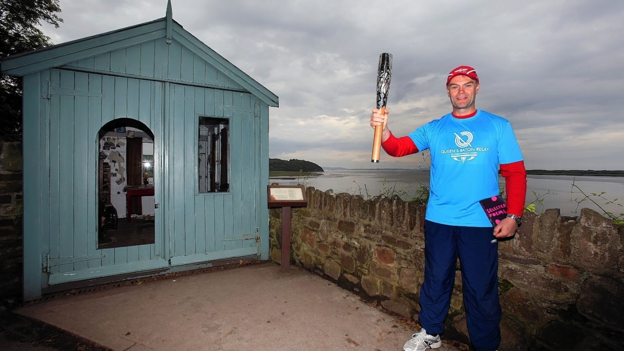 Baton Bearer Julian Lewis holding the Queen's Baton in front of the Dylan Thomas writing shed at Laugharne  in Wales. Wales is nation 68 of 70 nations and territories the Queen's Baton will visit