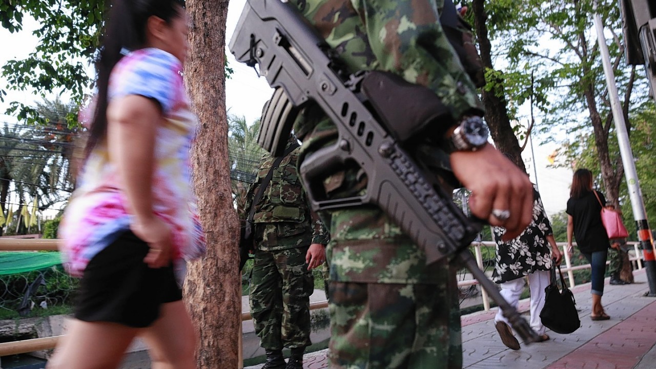 Pedestrians stroll past armed Thai soldiers guarding outside the Centre for the Administration of Peace and Order (CAPO) after soldiers were sent in to seize the center Tuesday, May 20, 2014 in Bangkok
