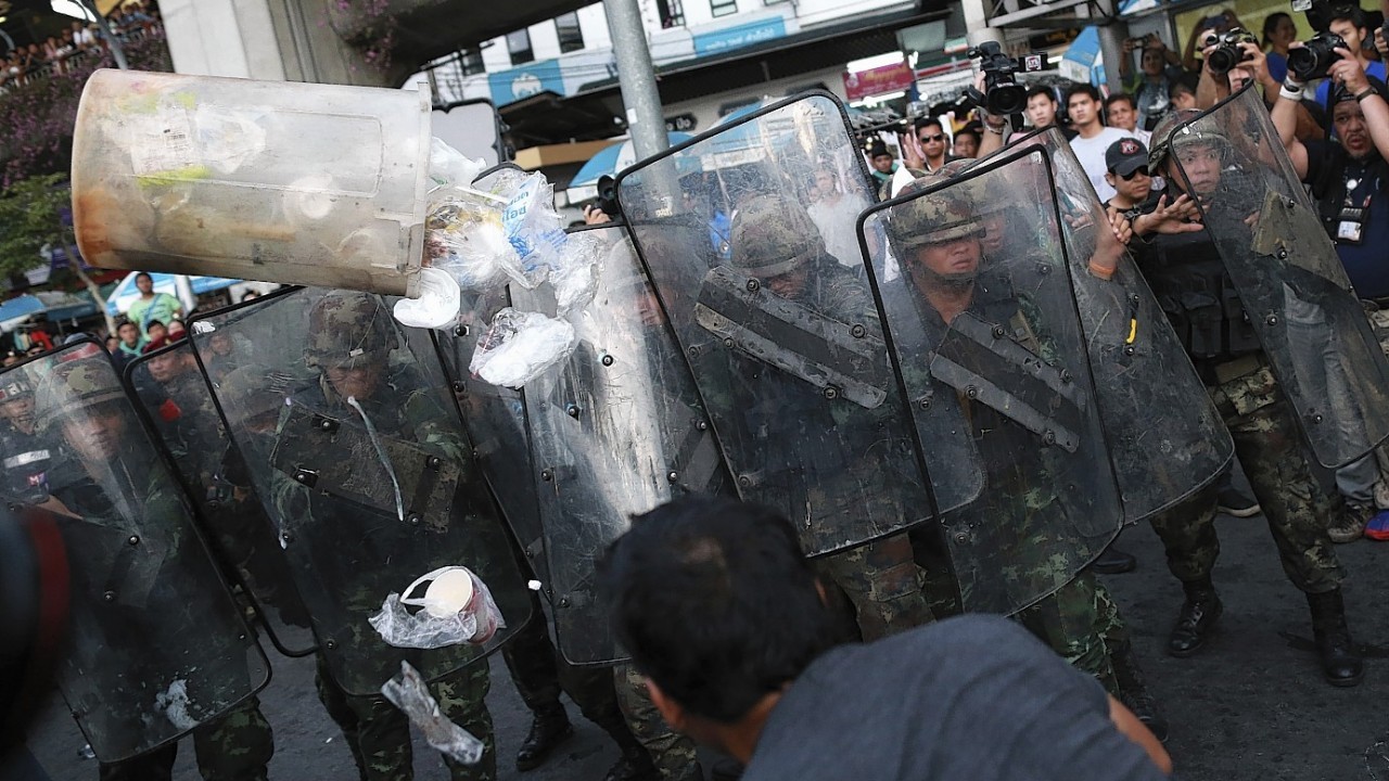 A protester, foreground, throws a garbage bin at a line of Thai soldiers during an anti-coup demonstration at the Victory Monument in Bangkok, Thailand Wednesday, May 28, 2014. Thailand's new military junta aired videos Wednesday on television stations nationwide showing some of the prominent political figures it has detained as part of an effort to convince the public that detainees in army custody are being treated well.
