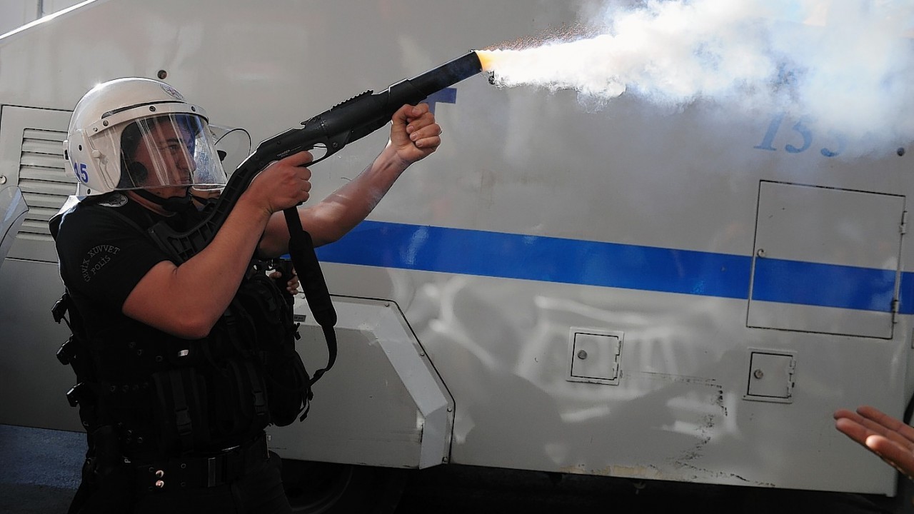 Riot police officer fires toward demonstrators who are protesting against the government in Soma