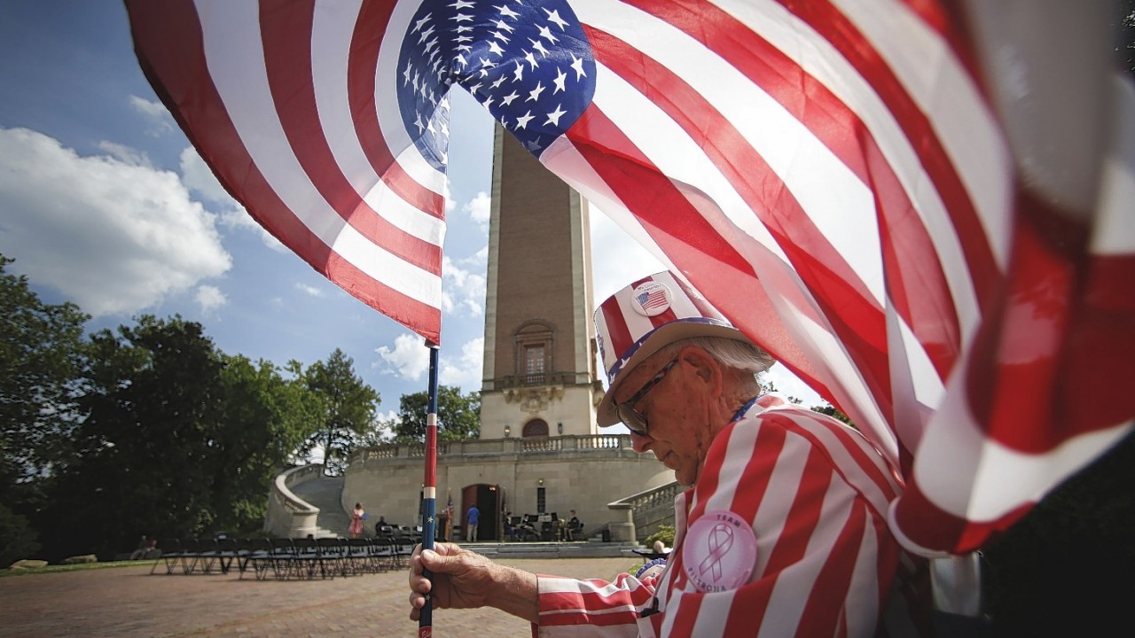 A breeze billows the American flag over the head of Tommy Sammons of Richmond as he waits for a military band concert to begin at the Carillon, a memorial dedicated to Americans who died in WWI in Richmond