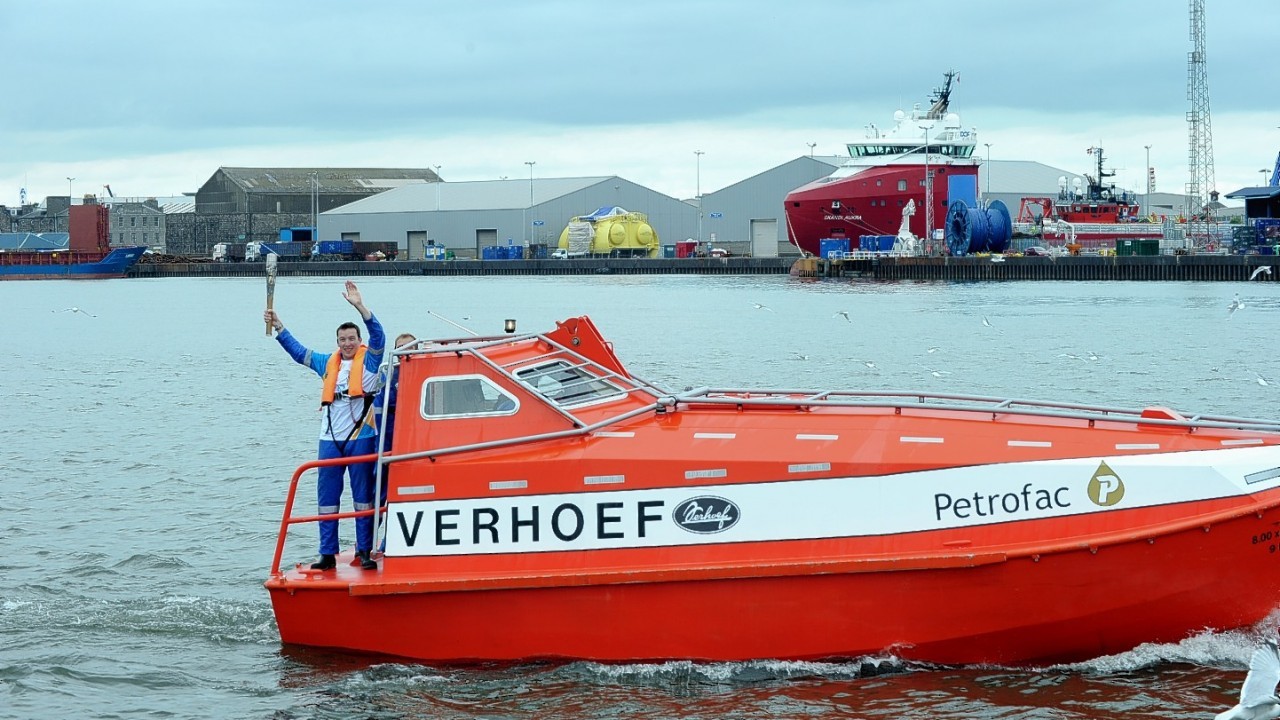 Colin Wallace takes the Queen's Baton Relay round Aberdeen harbour onboard Petrofac's freefall lifeboat.