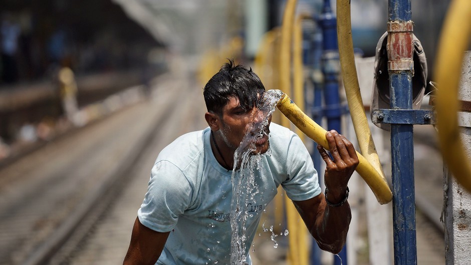 An Indian commuter splashes water from a pipe onto his face to get respite from the heat at the railway station in Allahabad. (AP)