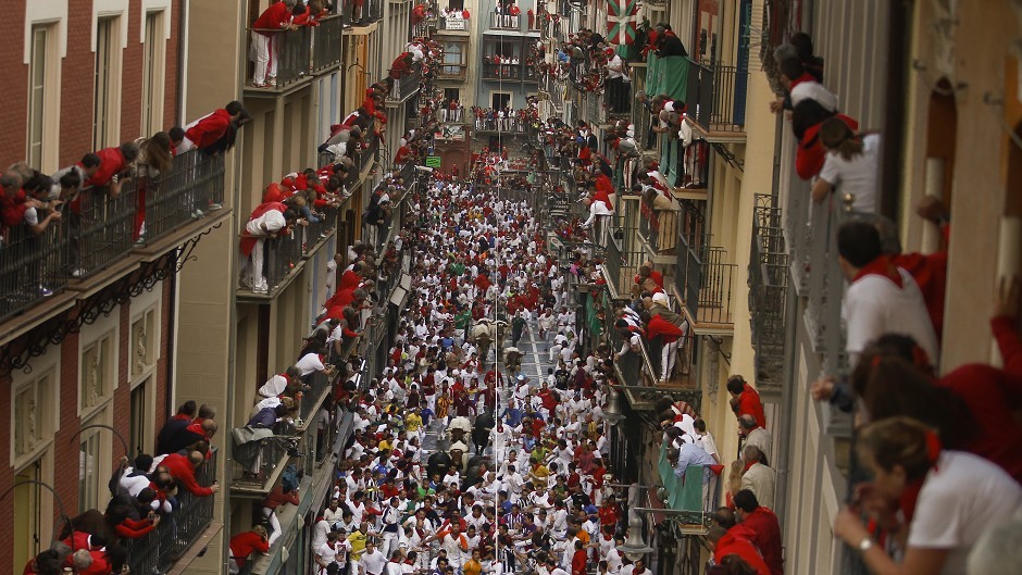 Jandilla fighting bulls run in between revellers as people watch from the balconies during the running of the bulls at the San Fermin festival in Pamplona, Spain (AP)