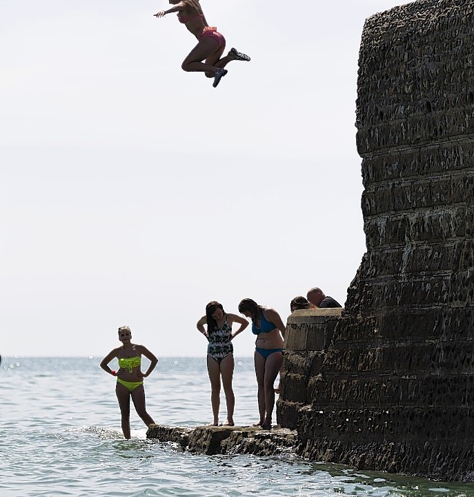 People jump off the sea defences into the water in Brighton, East Sussex as temperatures soar across the country