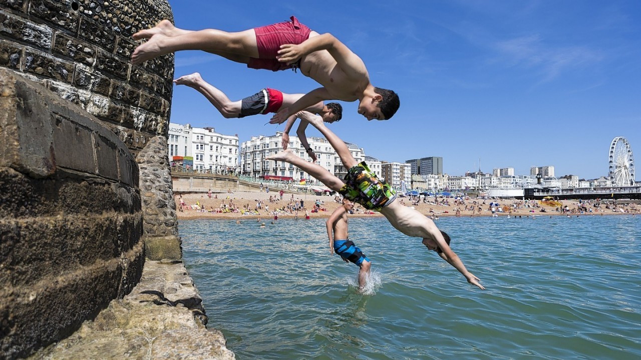 People jump off the sea defences into the water in Brighton, East Sussex as temperatures soar across the country