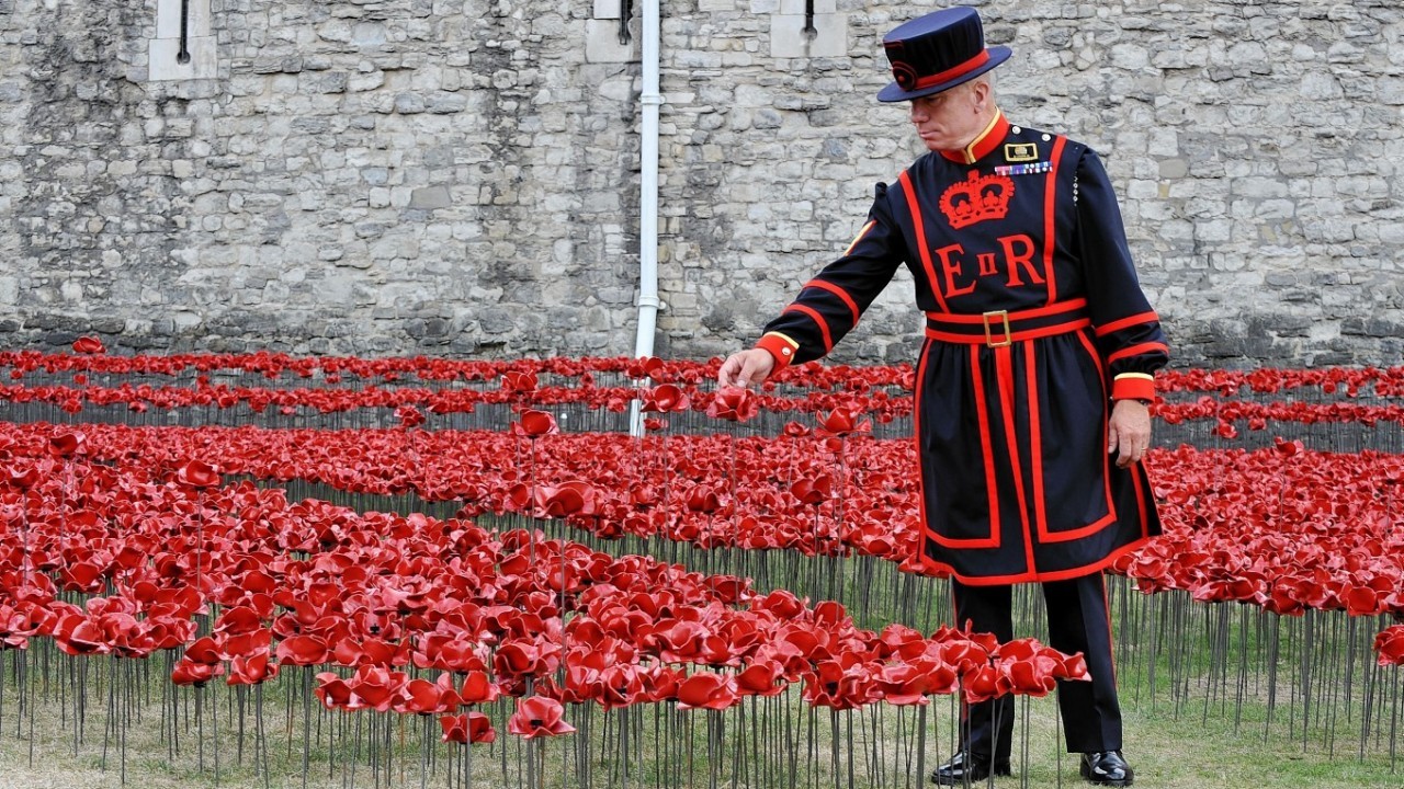 Yeoman Serjeant Bob Loughlin kneels by a mass of ceramic poppies which form part of the art installation 'Blood Swept Lands and Seas of Red' by artist Paul Cummins at the Tower of London