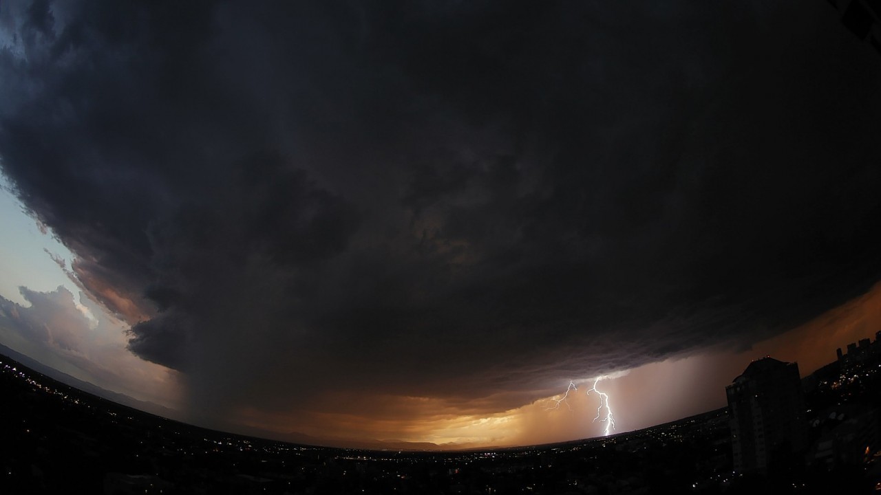 In this photo taken with a fisheye lens, a massive storm cloud packing high winds, hail and heavy rains sweeps over downtown Denver as lightning strikes on the horizon on Monday, July 7, 2014.