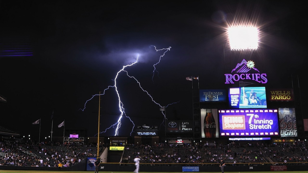Lightning strikes in the background during the seventh inning of an MLB baseball game between the Colorado Rockies and the San Diego Padres on Monday, July 7, 2014, in Denver.