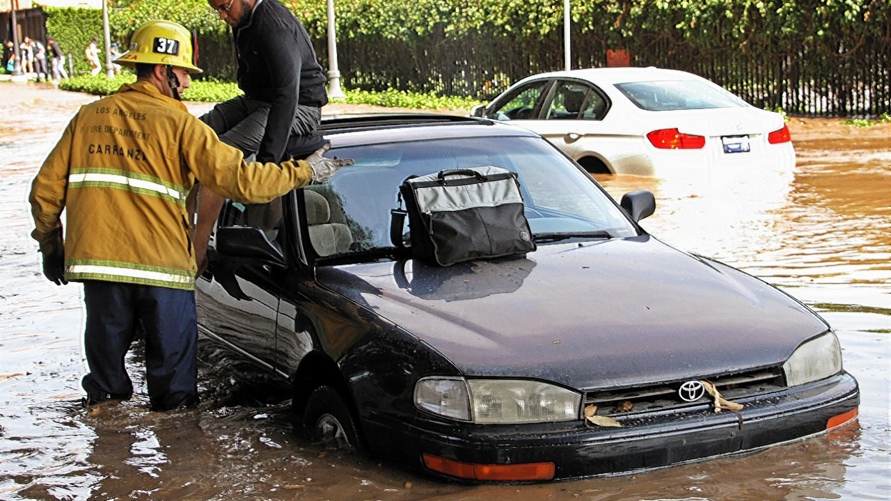 A Los Angeles firefighter helps a driver whose car became stranded on Sunset Boulevard after a 30-inch water main broke and sent water flooding down Sunset and onto the UCLA campus in the Westwood section of Los Angeles