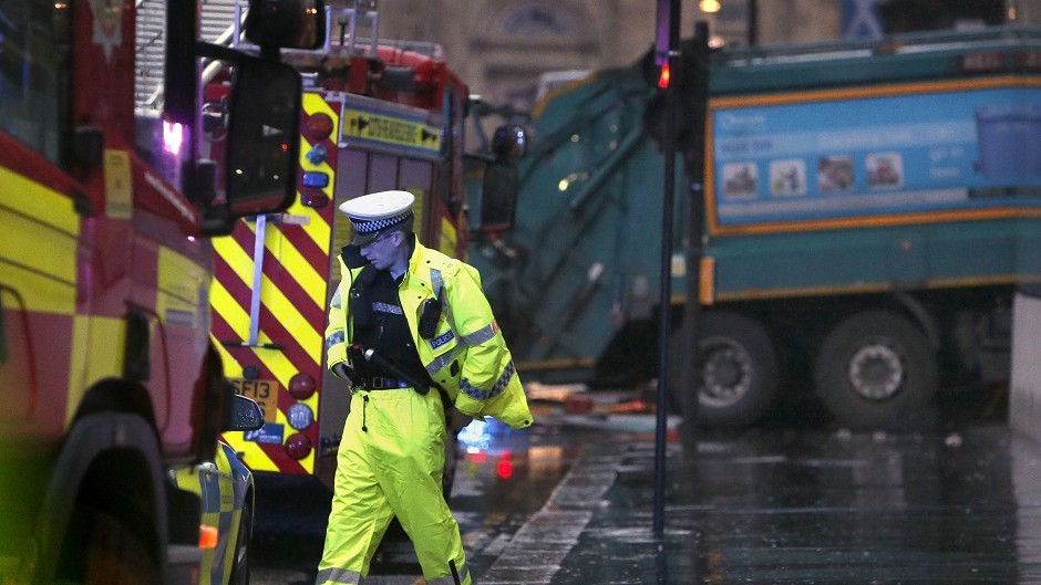 A police officer at the scene of the bin lorry crash in Glasgow. The lorry can be seen in the background.