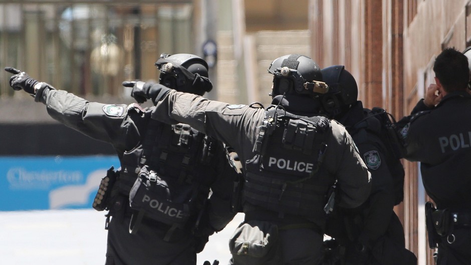 Armed police officers point as they stand at the ready close to a cafe under siege at Martin Place in Sydney, Australia (AP)