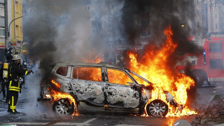 A firefighter extinguishes the flames of a burning police car after clashes between demonstrators and police in Frankfurt (AP) 