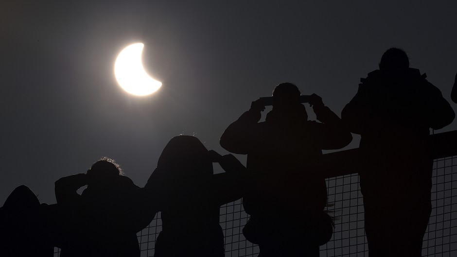 People watch as an eclipse of the sun begins over the Eden Project in Cornwall