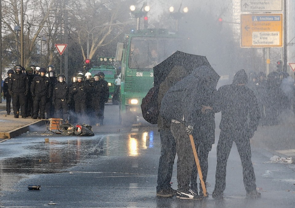 Masked protestors protect themselves against a water cannon 