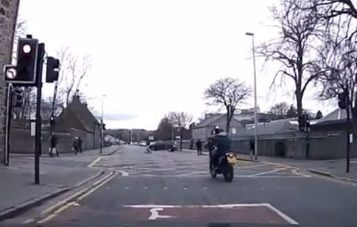 The footage shows a motorcyclist speeding through a red light without a helmet