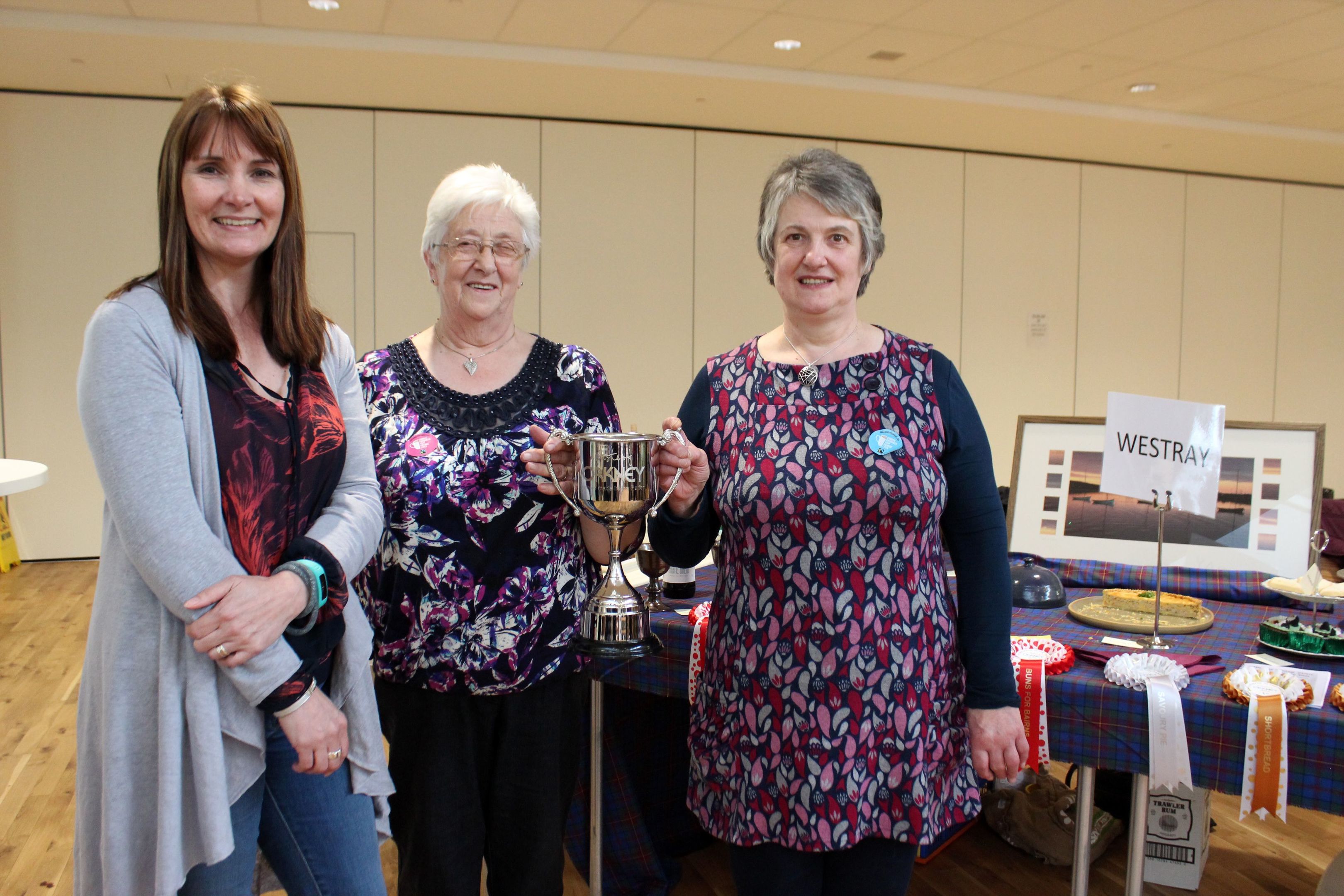 Westray representatives Ena Fergus (left) and Netta Harcus (right), receiving the Homemade in the Parish cup from OFD’s Fiona MacInnes (far left)