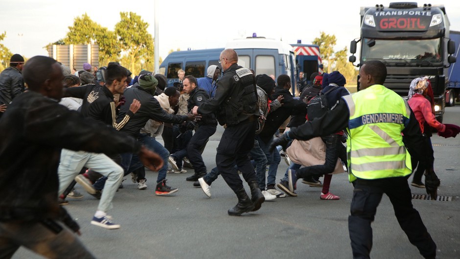 Migrants rush at a police cordon by a truck route along the perimeter fence of the Eurotunnel site at Coquelles in Calais, France.