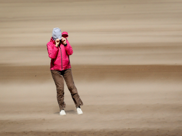 A woman walking on St Andrews beach shields her face from the sand, whipped up by the 40mph winds