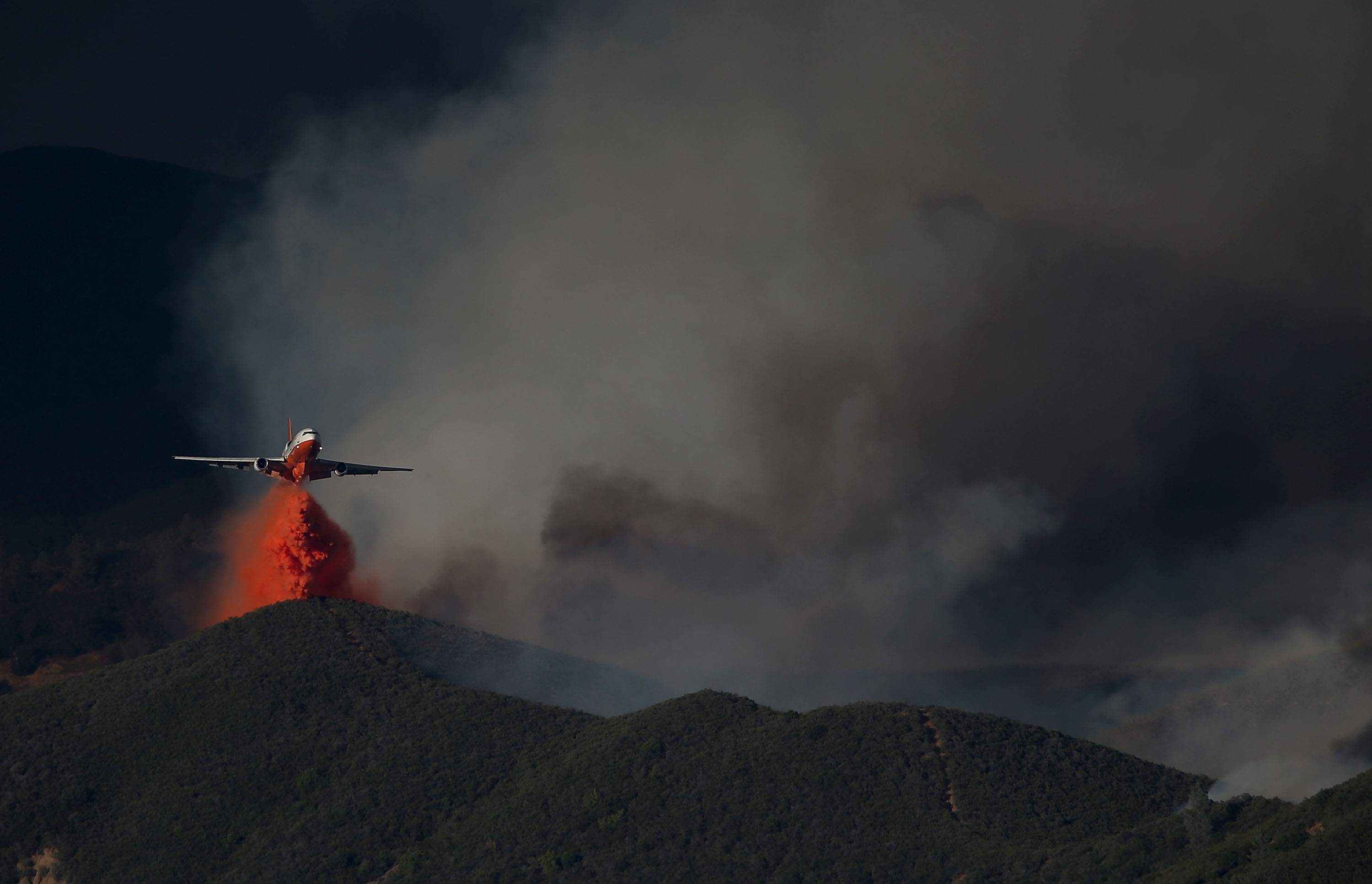 CLEARLAKE, CA - AUGUST 03:  A DC-10 firefighting aircraft drops fire retardant on a ridge in front of the Rocky Fire on August 3, 2015 near Clearlake, California. Nearly 3,000 firefighters are battling the Rocky Fire that has burned over 60,000 acres has forced the evacuation of 12,000 residents in Lake County. The fire is currently 12 percent contained and has destroyed at least 14 homes. 6,300 homes are threatened by the fast moving  blaze.  (Photo by Justin Sullivan/Getty Images) *** BESTPIX ***