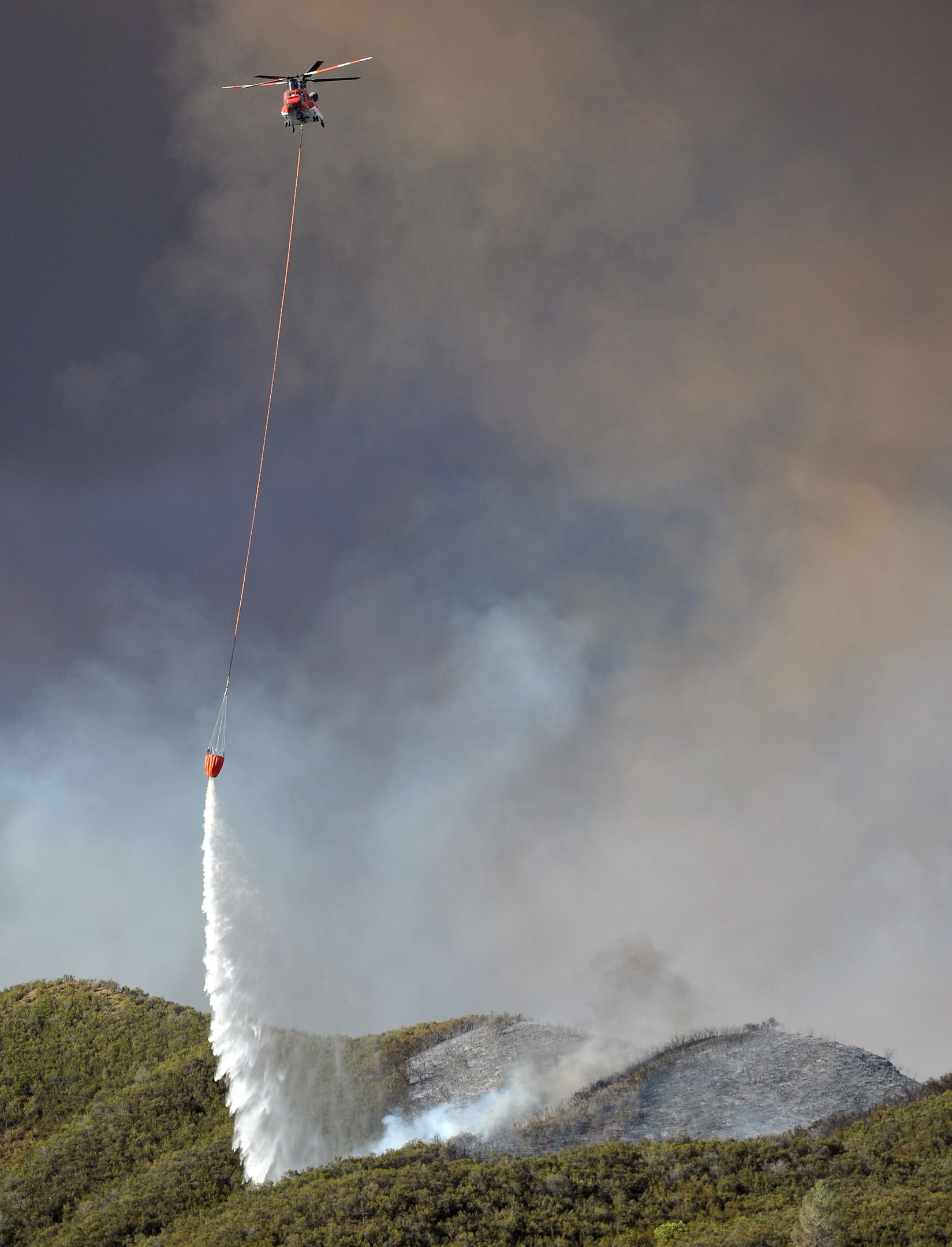 A helicopter drops water on a burning hillside while battling the Rocky Fire near Clearlake, Calif., on Monday, Aug. 3, 2015. The fire has charred more than 60,000 acres and destroyed at least 24 residences. (AP Photo/Josh Edelson)