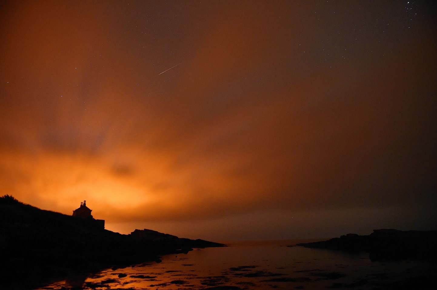 A shooting star seen through thin cloud in the skies over the Bathing House at Howick in Northumberland