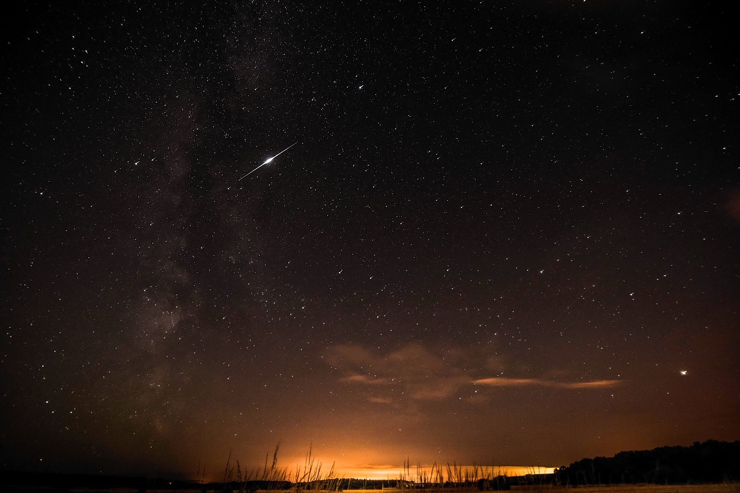 A meteor appears to pass through the Milky Way during the annual Perseid meteor shower, in Moray
