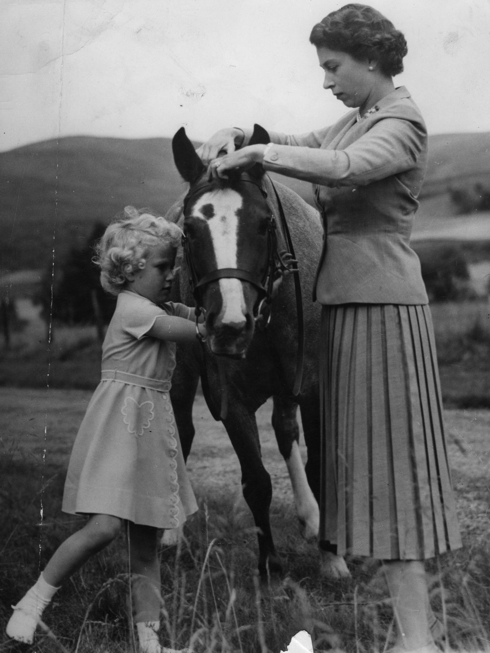 1955 of Princess Anne helping her mother, Queen Elizabeth II, fit the bridle to the pony 'Greensleeves', the the grounds of Balmoral Castle during the Royal family's summer holiday in Scotland.