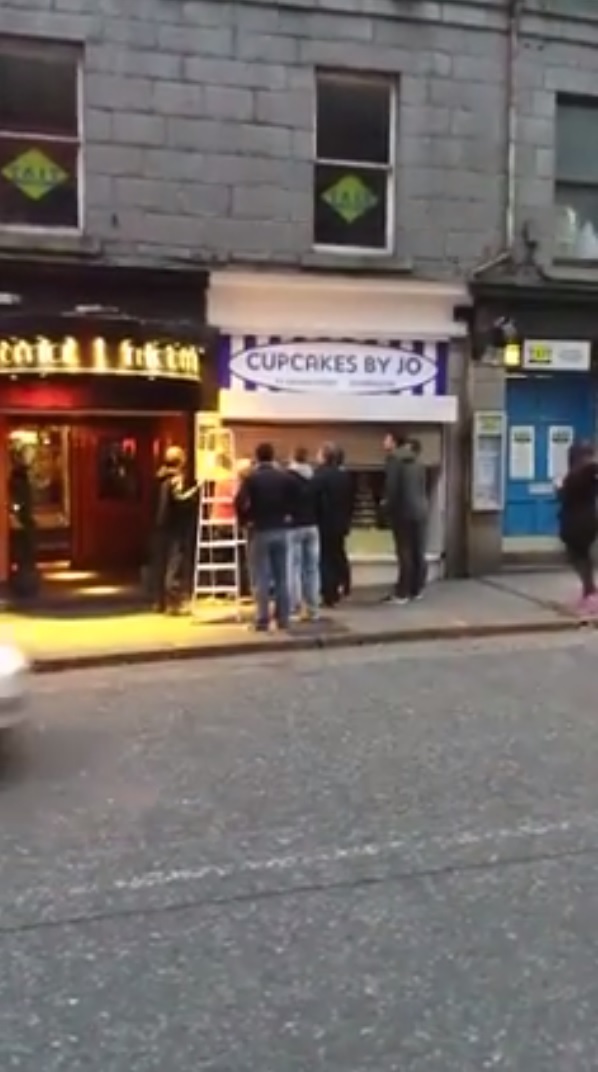 Ten fully grown men take time out of there day to help pull the shutters down on a cupcake shop