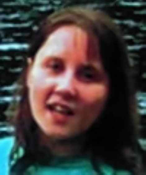 A woman in her twenties with with brown hair to her shoulders looks at the camera in a blurry image